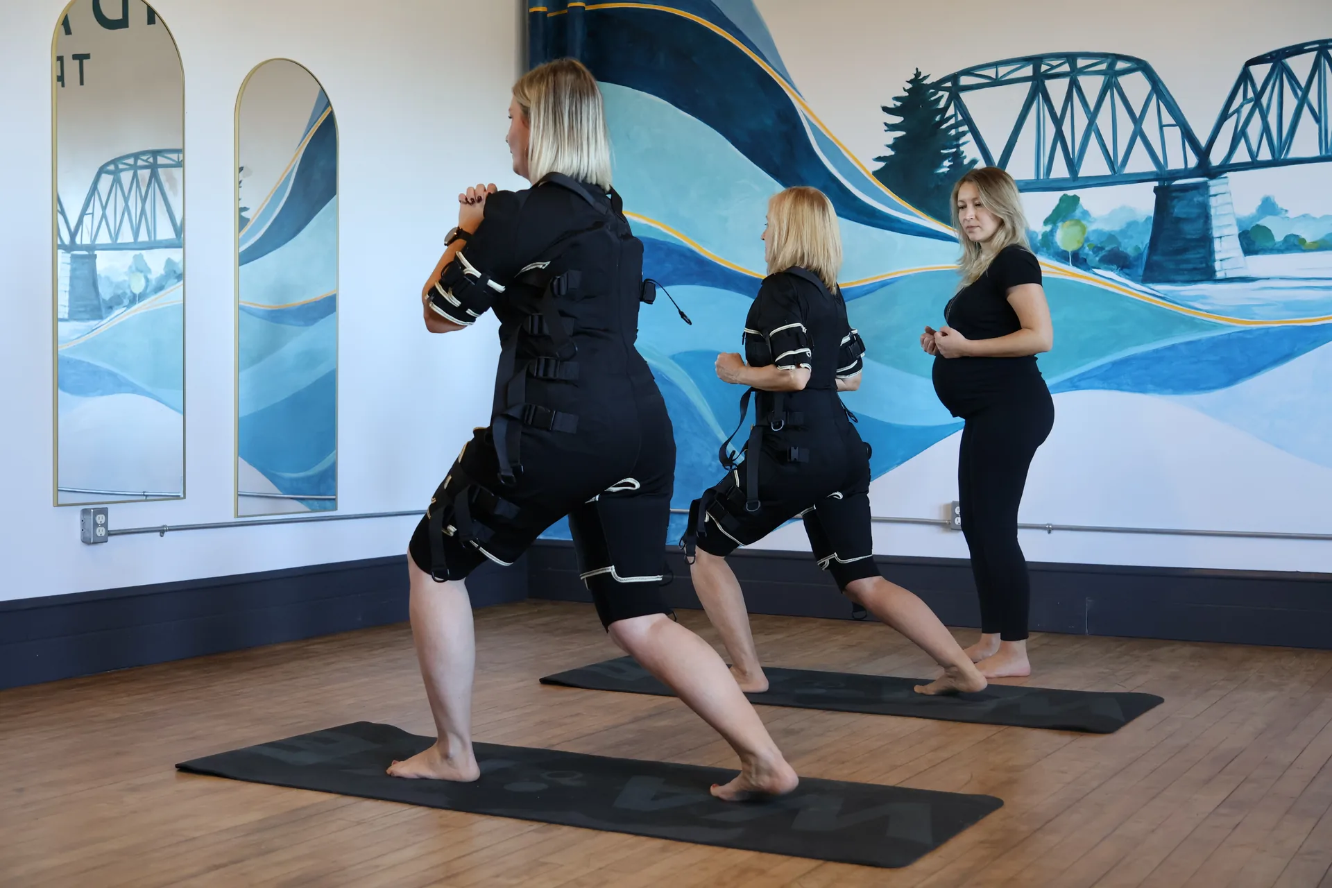 Two clients practising movements in EMS suits with their coach in the Tidal Signal studio